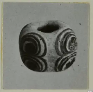 Bead with concentric banded rings on several faces and a large hole through the top, shown on a grey card.