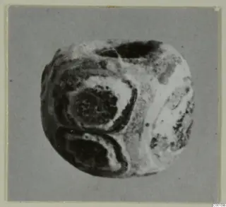 Close photograph of a rounded object with a hole near the top and dark oval banding across its surface