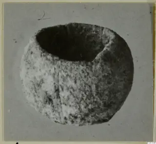 Bone bead from Ayia Irini, a rounded object with a large opening on top, photographed on grey
