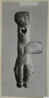 Stone idol with a rounded head, a hole pierced through the upper body and a side projection, photographed on grey card
