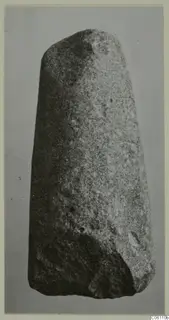 Tapering stone object with a rounded top, photographed against a grey background