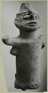 Terracotta figure from Ayia Irini with a cylindrical body, stub arms and a modelled face, seen against a plain grey background