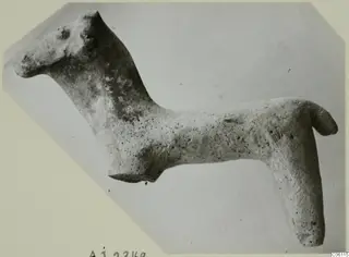 Terracotta figurine of a standing animal with a long neck and upturned tail, photographed in side view.