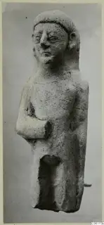 Terracotta statuette of a standing figure with one arm bent across the body, shown against a plain grey backdrop