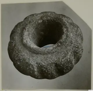Stone macehead with a scalloped outer edge and a large central perforation, photographed from above