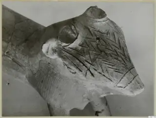 Close-up of a terracotta figurine's head with a pointed snout, a rounded knob and incised chevron patterns on its surface
