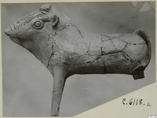 Terracotta animal figure in side view, with incised zigzag lines on the head and a long projecting stub below the body