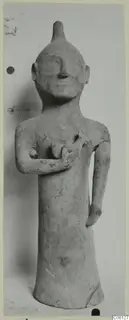 Terracotta statuette of a standing figure with a pointed head, one arm bent across the chest holding a small object.