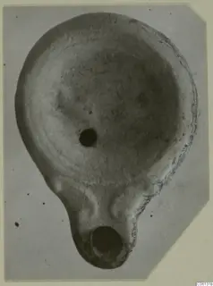 Terracotta oil lamp seen from above, with a filling hole and a round nozzle at the lower end.