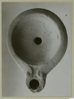 Terracotta oil lamp with a round filling hole on top and a nozzle at the bottom, shown from above.