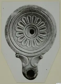 Terracotta oil lamp with a radiating petal pattern on its round disc and a handle at the base.