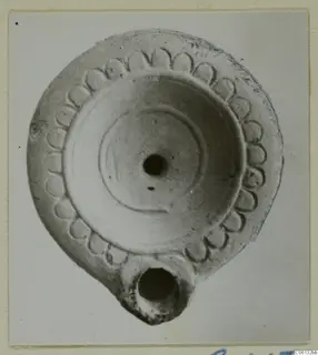 Terracotta oil lamp seen from above, with a ring of leaf-like petals around the rim and a filling hole.