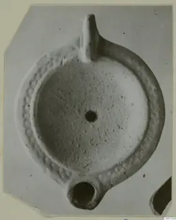 Terracotta oil lamp with a upright handle and a round filling hole, seen from above.