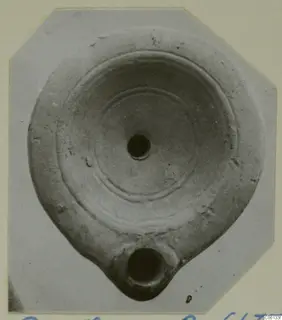 Terracotta lamp seen from above, with concentric rings on its disc and a nozzle with a round opening at the bottom.