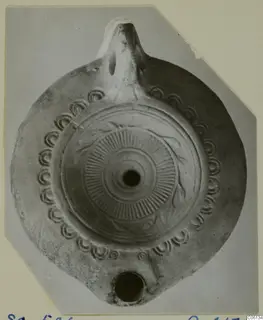 Terracotta oil lamp viewed from above, with a ring of impressed scrolls around the rim and a radiating pattern on the disc.