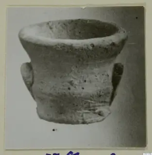 Small plain pottery cup with a rounded body, flared rim and two small handles, photographed on a light background.