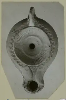 Terracotta oil lamp seen from above, with a radial ribbed disc, a pattern border and a nozzle at the top.