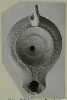 Terracotta oil lamp seen from above, with a nozzle at the top, a handle at the bottom and a central filling hole.