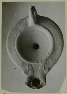 Terracotta oil lamp with a handle, seen from above, with a central filling hole and a nozzle at the bottom.