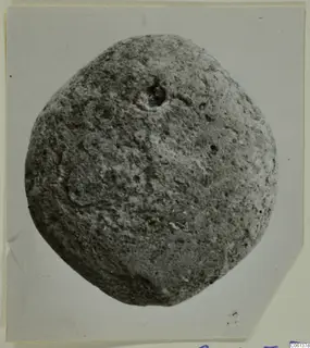 Terracotta loom weight, rounded and pitted, with a hole near the top.