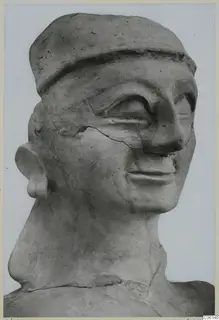 Bust of a figure with a flat cap-like headdress, large eyes and a cracked surface, seen in close view against a plain background