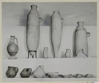 Pottery vessels from Tomb 16 at Vouni: jars, jugs and bowls set out in two rows against a pale backdrop.