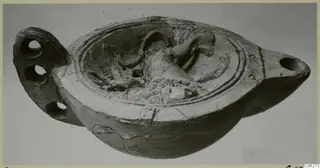 Terracotta oil lamp with a raised relief scene on its disc and a flat pierced handle at the left