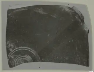 Pottery sherd with concentric ring decoration in its lower left, photographed on a grey card mount