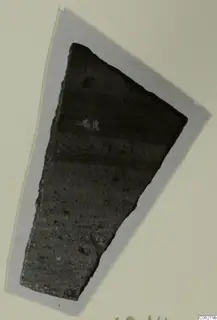 Wedge-shaped pottery sherd, dark grey with horizontal bands, shown on a grey card mount.