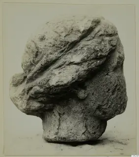 Stone head sculpture from Soli, seen from the side, with carved bands across the top of the head and worn features