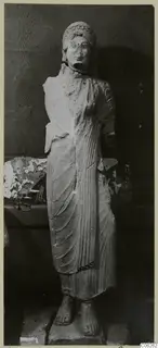 Limestone statue of a standing female figure from Vouni, in a long draped garment, shown against a dark background.