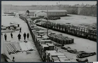 Railway wagons and stacked wooden crates along the quay at Famagusta harbour, with men standing among them