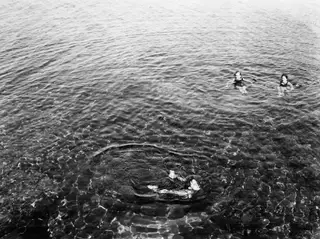 Three people swimming in clear sea water at Kyrenia, seen from above.
