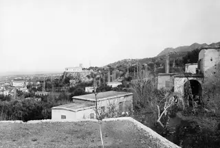 View from the village of Lapithos over white houses, a whitewashed church on a rocky knoll, and hills beyond.
