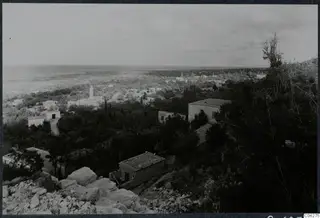 View over the village of Lapithos towards the sea, with white houses scattered among trees on the slope.