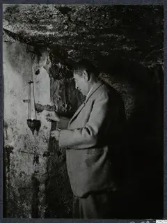 Perides lighting a small hanging lamp in a rock-cut chamber at Kition, Larnaca