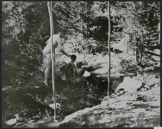Two men bathing in the forest at Machairas, one standing by a tree trunk and one seated in a tub