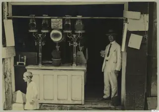 Juice stall in Nicosia with glass jars on metal taps, and a man in a light suit holding a glass in the doorway