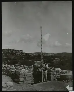 Man holding a tall measuring rod beside stone walls at Nitovikla