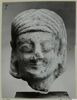 Limestone head sculpture from Kition, with ridged hair bands and lowered eyes, shown on a dark stand