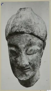 Limestone head from Kition with a rounded cap and lowered eyes, photographed frontally.