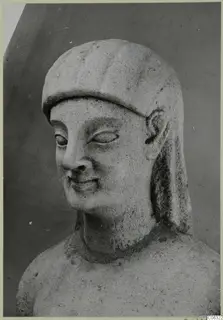 Limestone head from Kition, turned slightly to one side, with a close-fitting head covering and a faint smile.