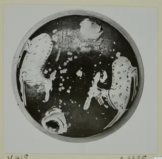 Interior of a shallow round pottery vessel seen from above, with dark glaze and pale painted motifs