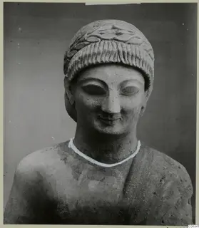 Limestone sculpture head and shoulders from Kition, with a carved leaf-patterned headdress and downcast eyes