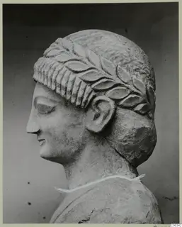 Limestone head in profile facing left, with a carved band of leaves across the hair above the forehead