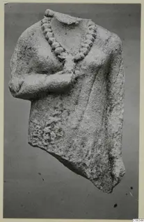 Limestone statue fragment of an upper body with a carved bead necklace and one arm bent across the chest