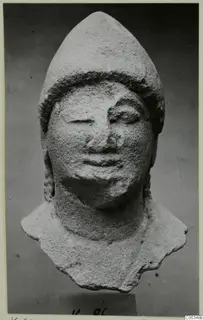 Limestone head fragment from Kition with a tall pointed cap, shown frontally on a small block base