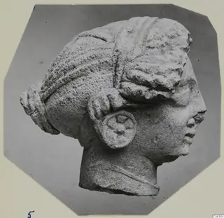 Limestone head fragment from Vouni, shown in right-facing profile against a grey backdrop