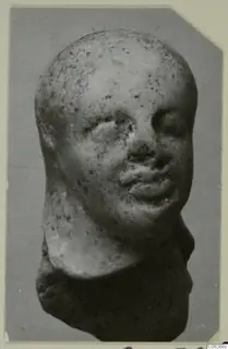 Terracotta figurine head from Vouni, photographed against a grey background