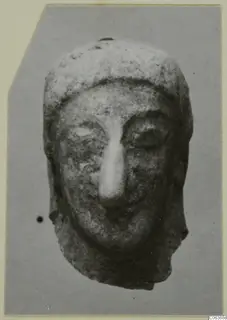 Head of a small terracotta figurine with a long straight nose and deep-set eyes, from Vouni, shown against a grey backdrop